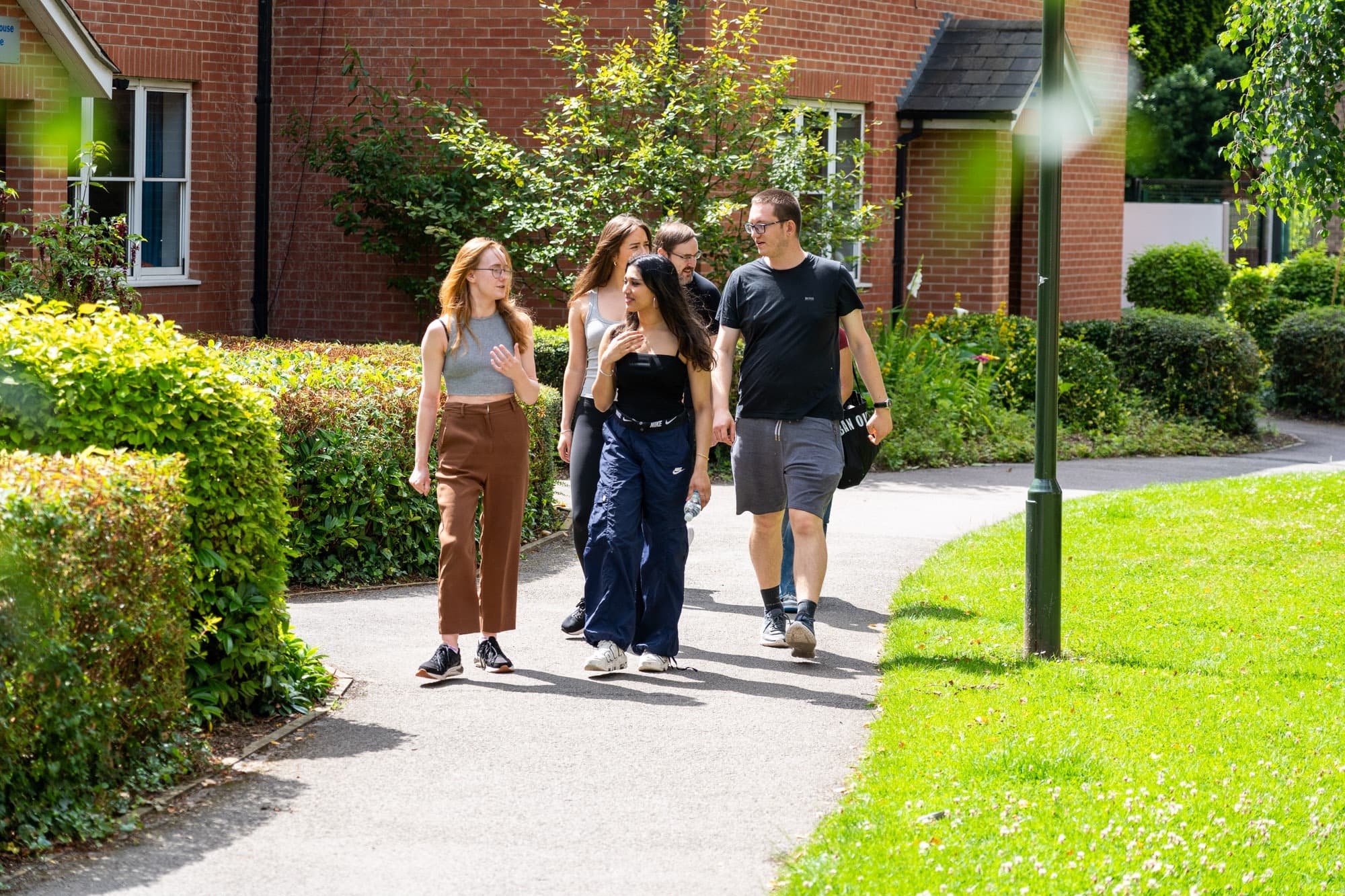 Students walking along a tree-lined path between the brick accommodation blocks